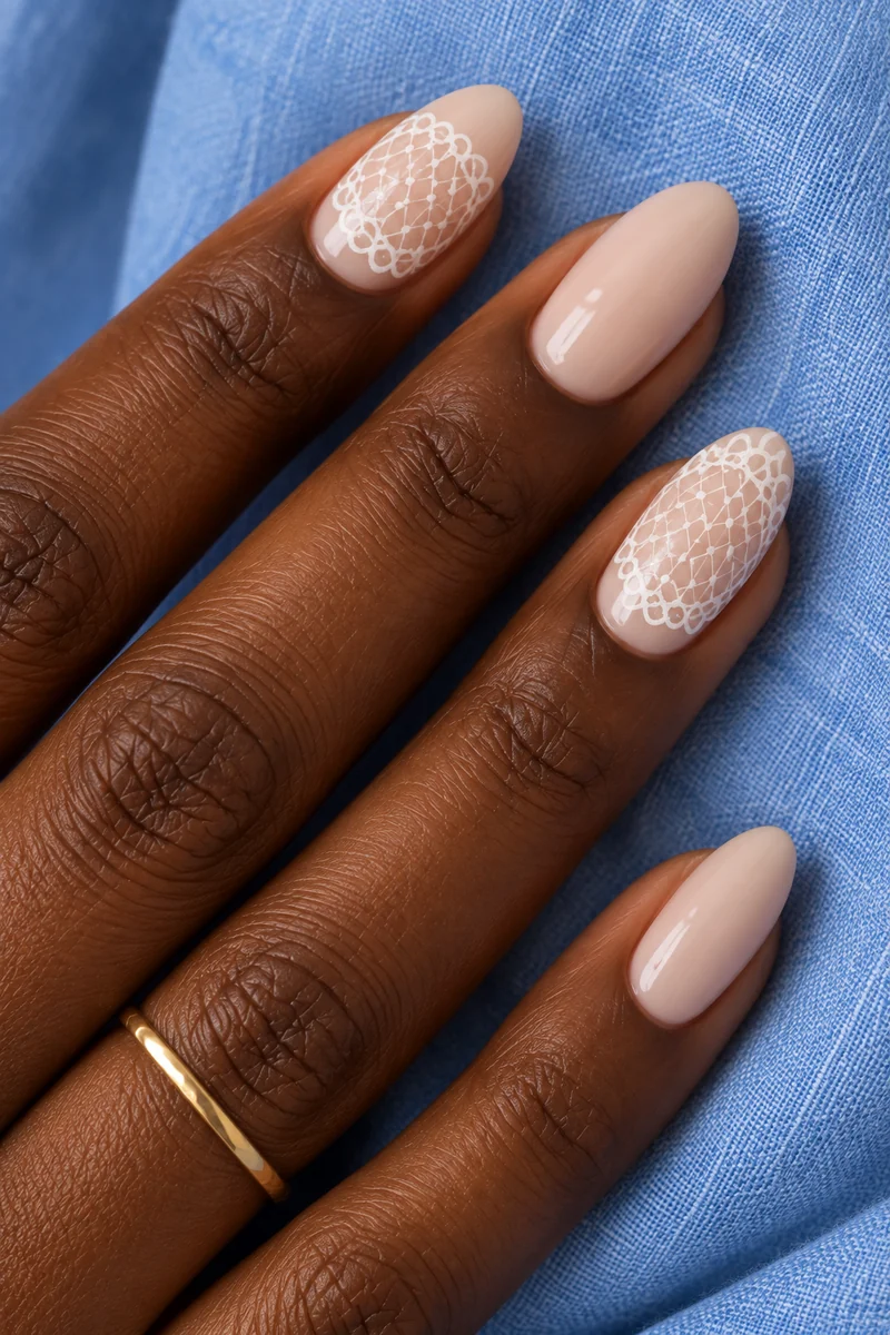 Beige almond nails with two ivory crochet-inspired lattice accents in close-up against a blue shirt