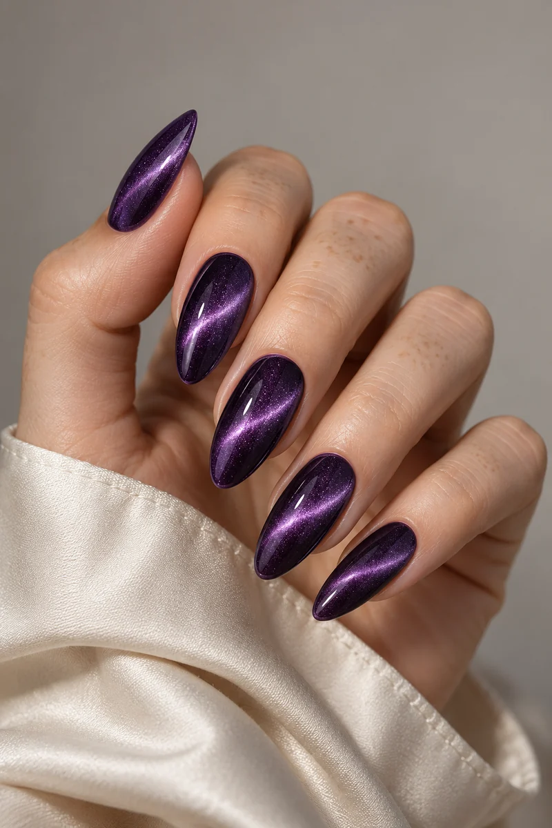 Long almond purple cat-eye nails with bright diagonal lavender bands beside an ivory satin cuff