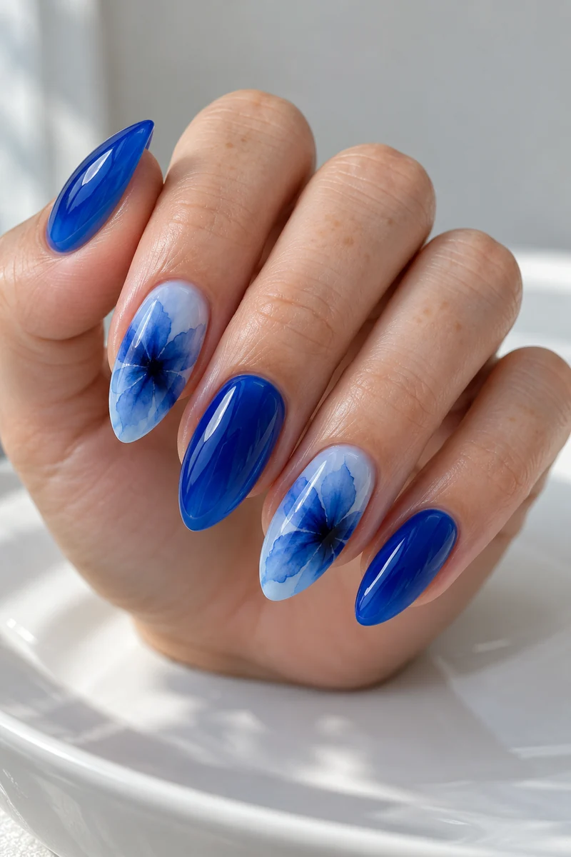 Medium almond nails in blue jelly with diffused cobalt blooming-flower accents on pale skin