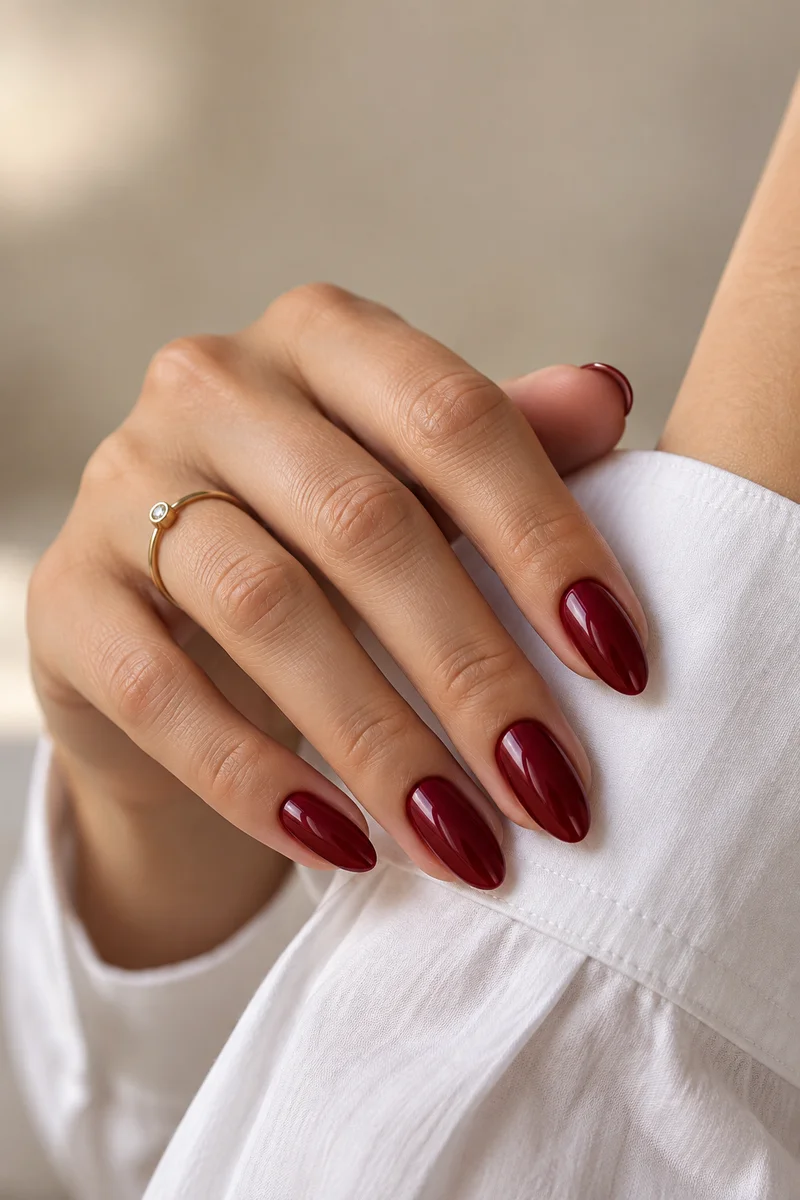 Glossy wine red almond manicure beside a white shirt cuff